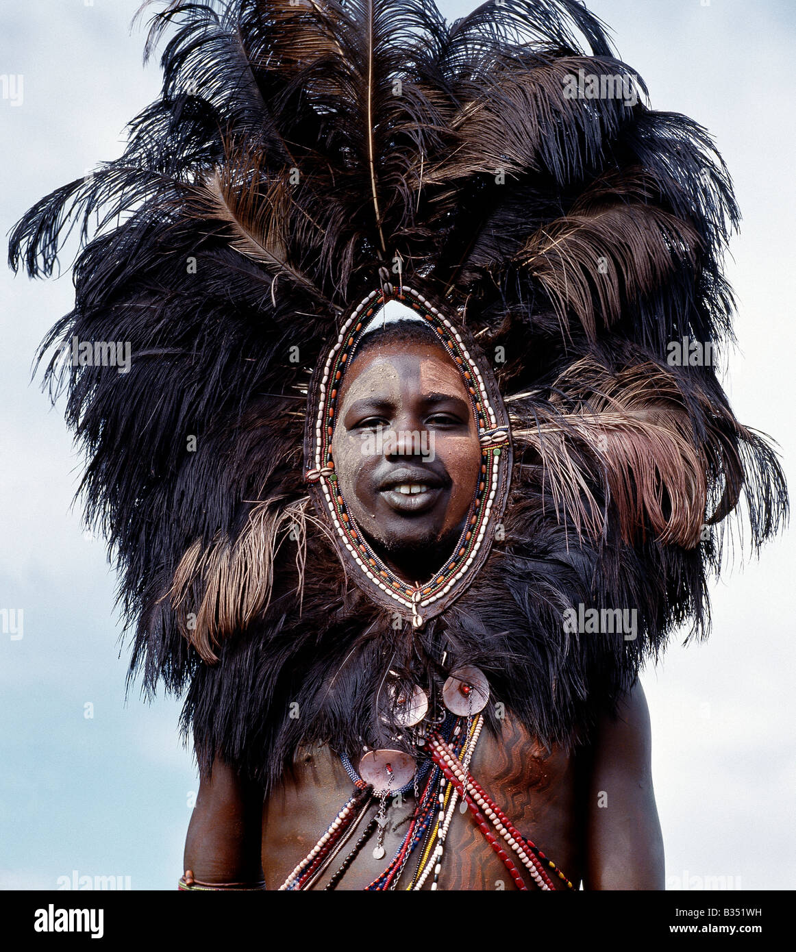 Kenya, Trans-Mara, Lolgorien. Un guerrier Masaï, son visage et corps décoré d'ocre rouge et d'argile, porte une coiffe de plumes d'autruche. Cette parure singulière a été une fois porté par les guerriers allant au combat et était probablement destiné à effrayer l'ennemi. Banque D'Images