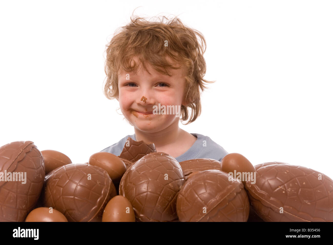 Jeune enfant avec du chocolat sur son nez émergeant de derrière une grosse pile d'oeufs de Pâques Banque D'Images