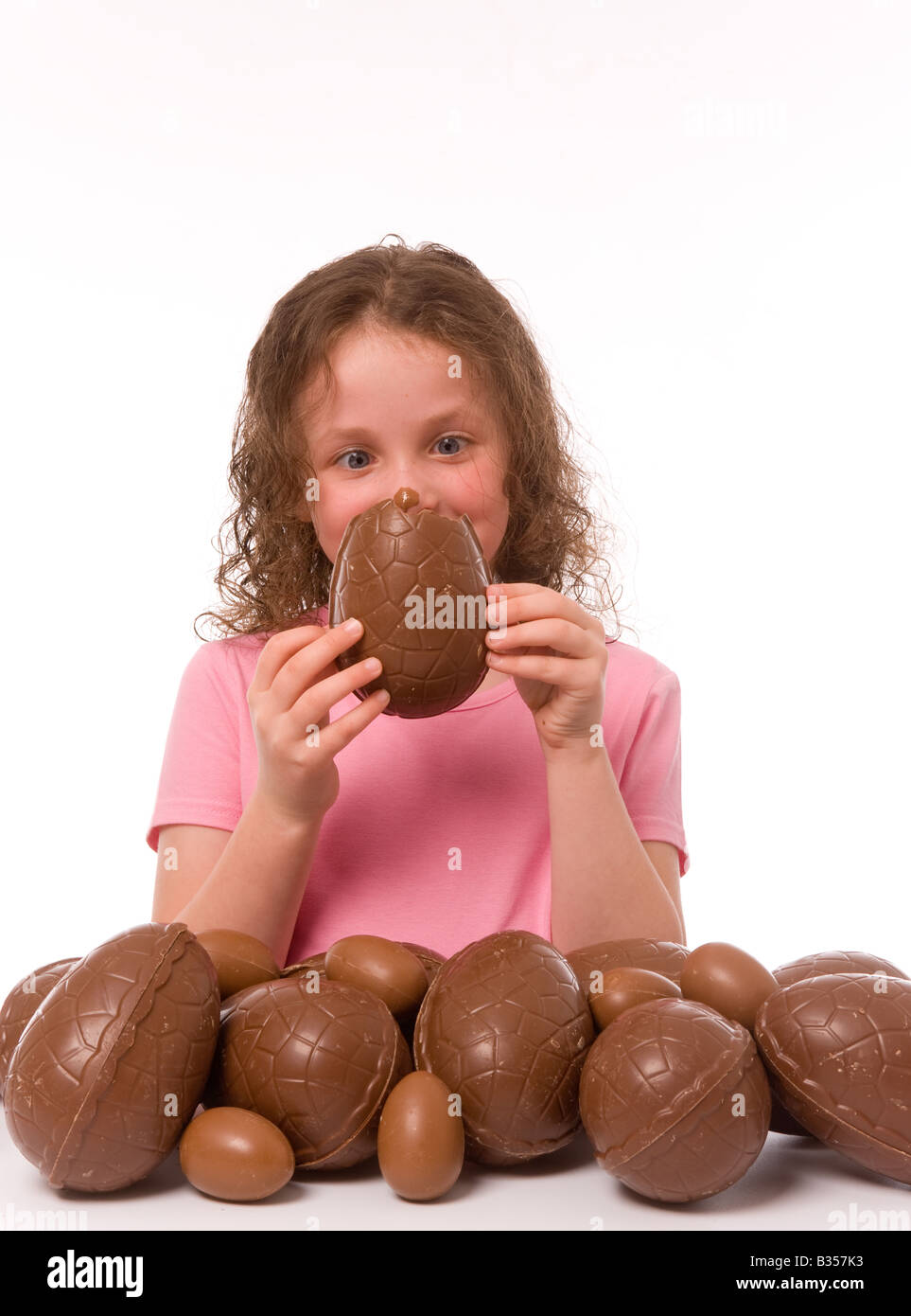 Jeune enfant qui est à la tête d'un morceau d'oeuf de Pâques qu'elle tient devant son visage recouvert de chocolat. Banque D'Images