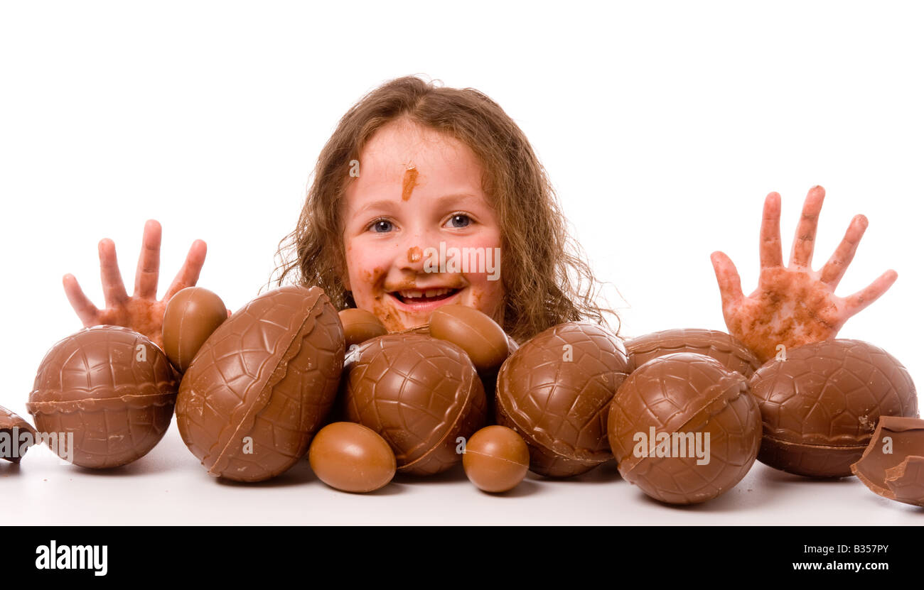 Jeune enfant avec une grosse pile d'oeufs de pâques avec les mains et le visage recouverts de chocolat. Banque D'Images