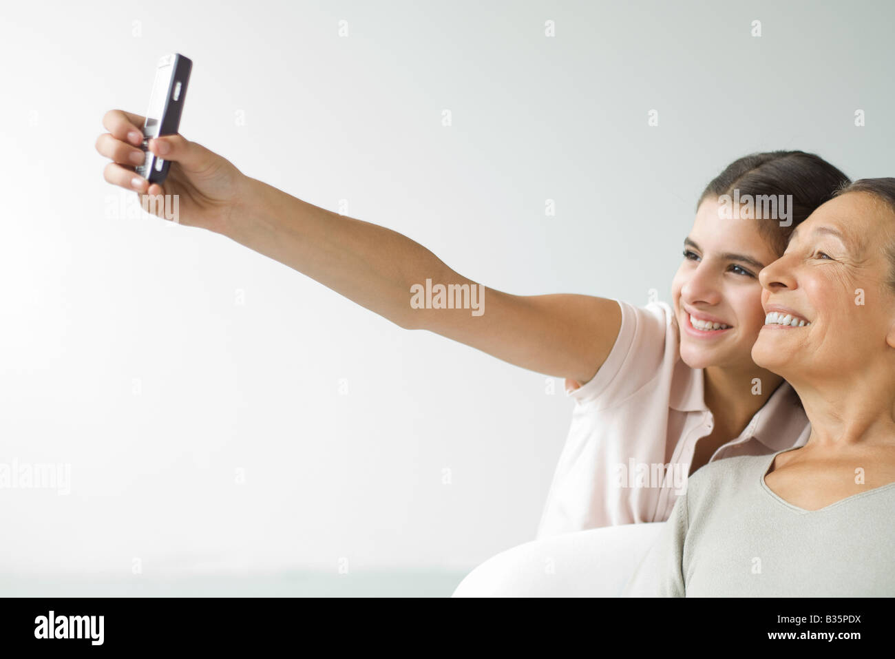 Teenage girl growing et grand-mère avec un téléphone cellulaire, les deux smiling Banque D'Images