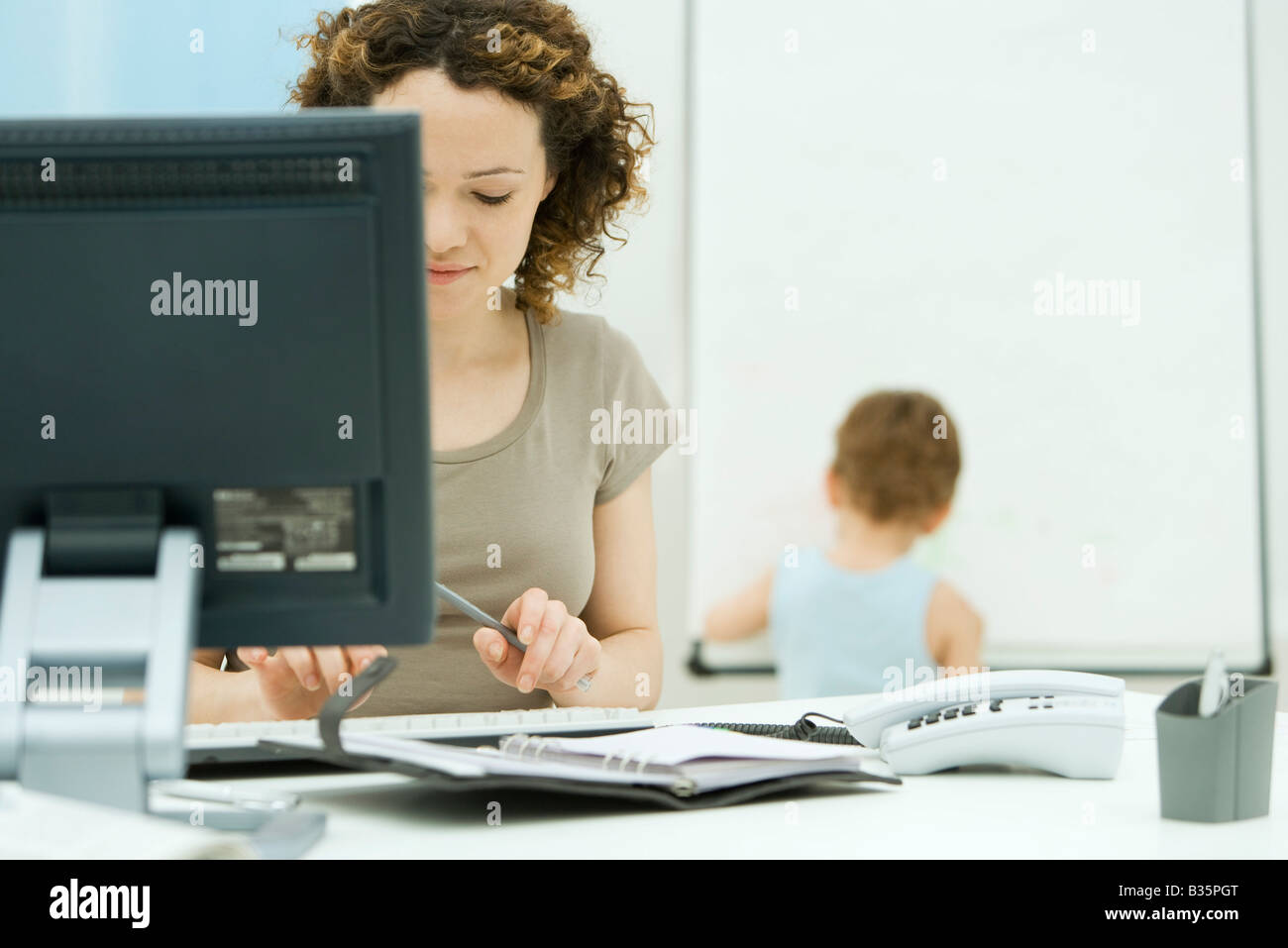 Femme travaillant à l'ordinateur de bureau à la maison, jeune fils jouant en arrière-plan Banque D'Images