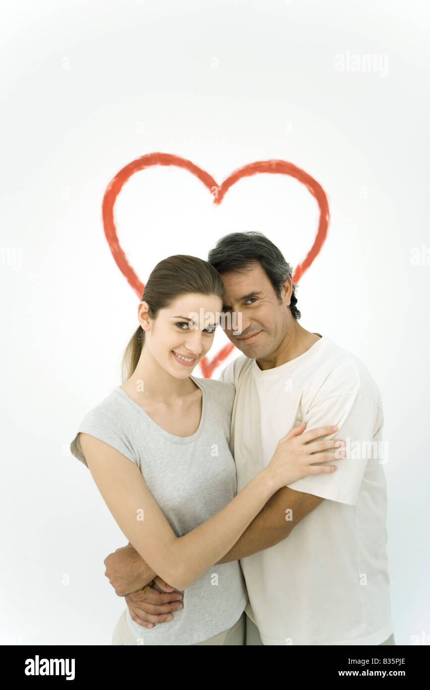 Couple hugging devant coeur peint sur mur, smiling at camera Banque D'Images