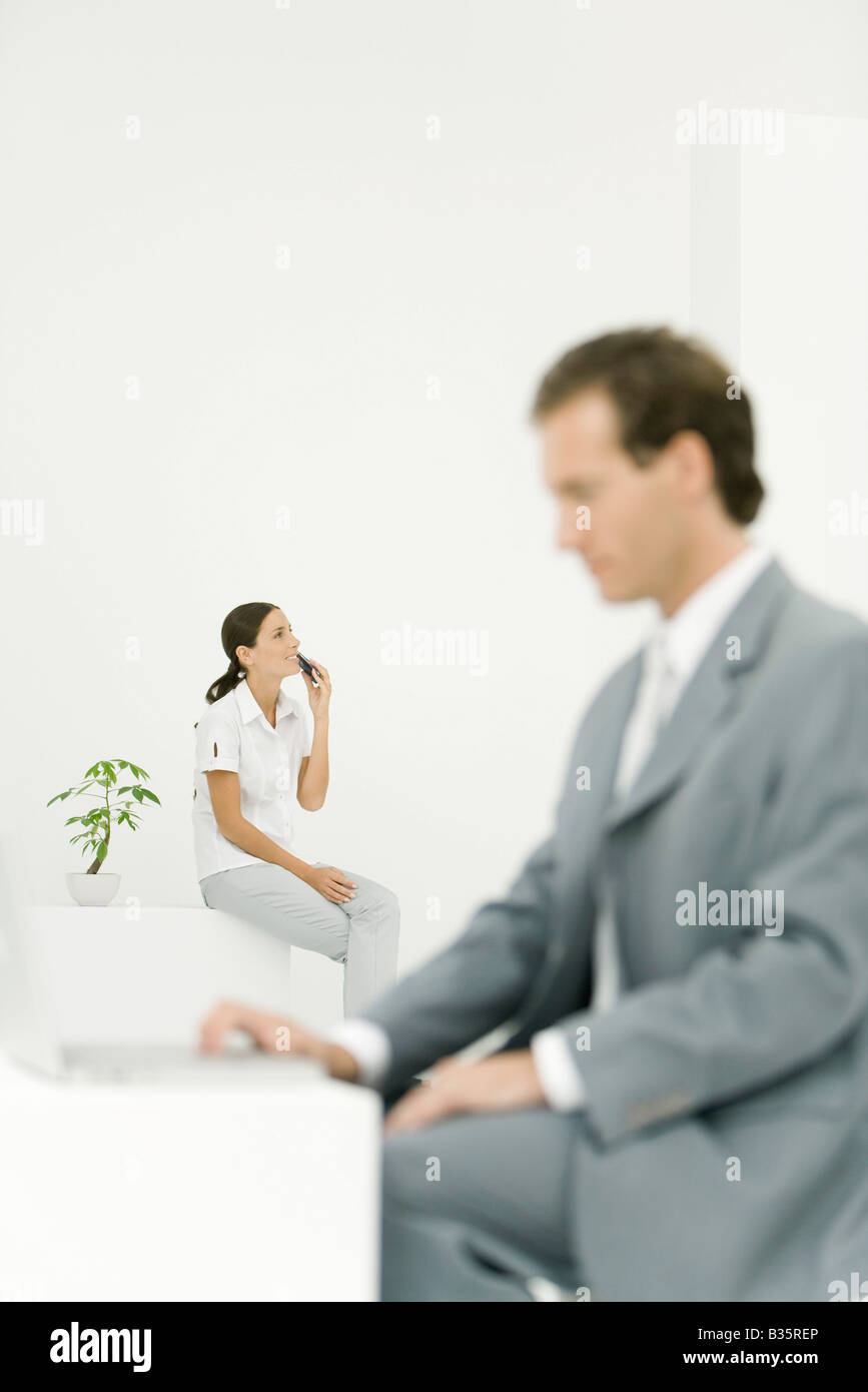 Jeune femme assise avec téléphone cellulaire, ordinateur portable professionnel à l'aide de l'homme en premier plan Banque D'Images