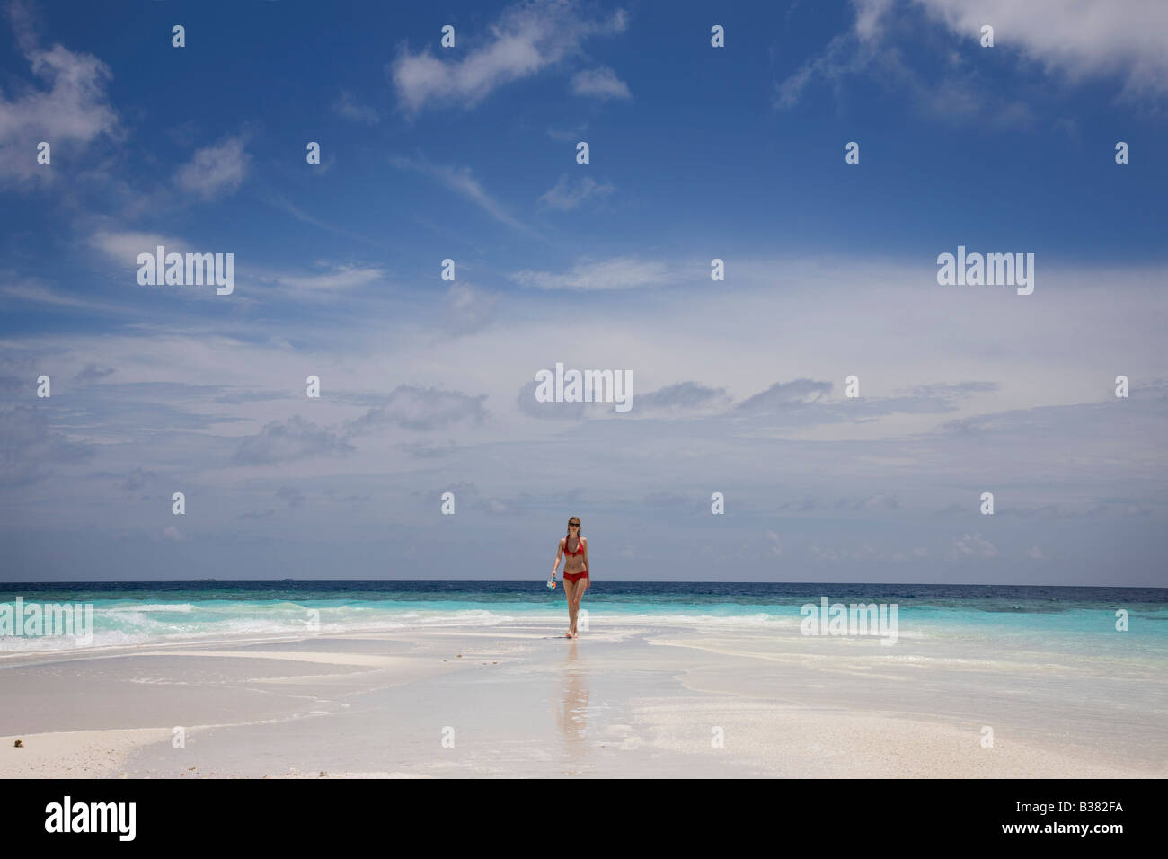 Jeune femme marchant le long de la plage de sable blanc déserte entourée par les eaux tropicales près de l'Inde aux Maldives Banque D'Images