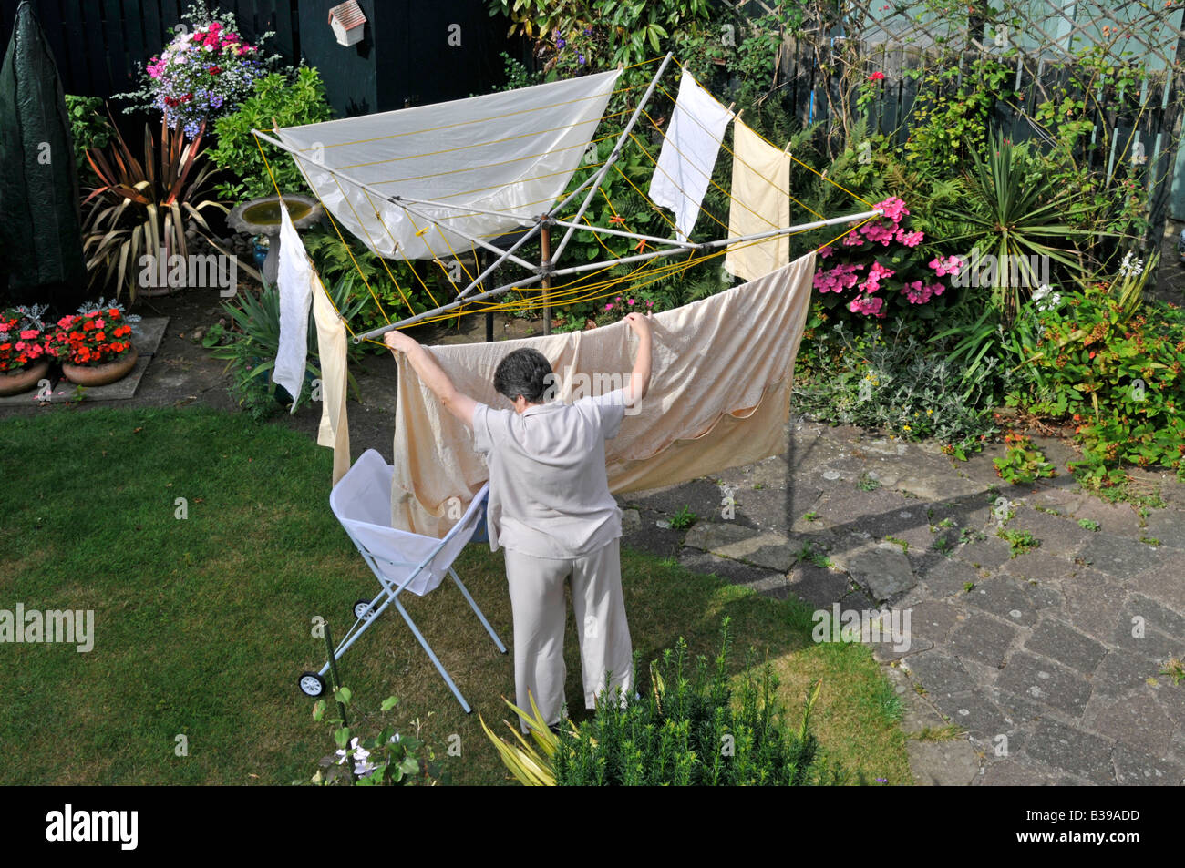 Jardin à l'arrière et pelouse de la propriété résidentielle vue aérienne mature femme séchée sur une ligne de vêtements rotative pour sécher au soleil Angleterre Banque D'Images