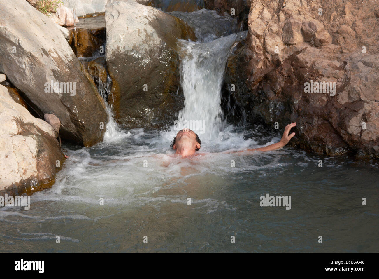 Un randonneur mâle se rafraîchi sous une petite cascade de montagne. Banque D'Images