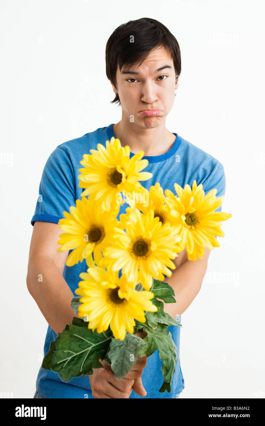 Asian young man holding bouquet de marguerites jaunes avec gerber moue sur son visage Banque D'Images