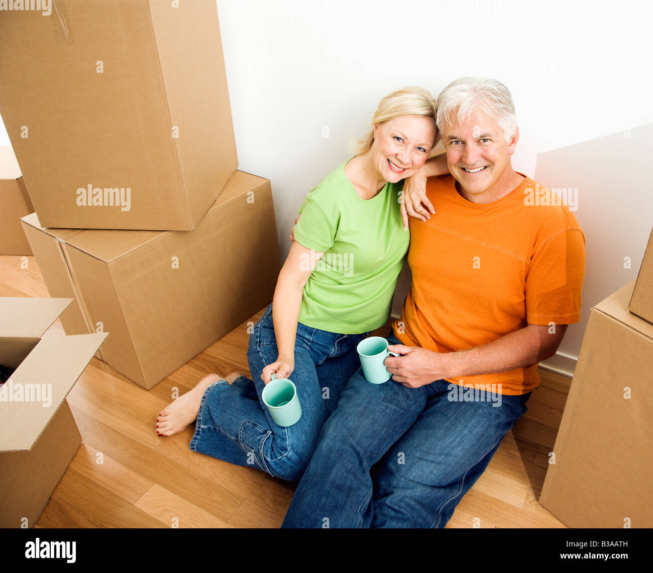Couple d'âge moyen assis sur le plancher entre les cartons de déménagement en carton avec du café Banque D'Images
