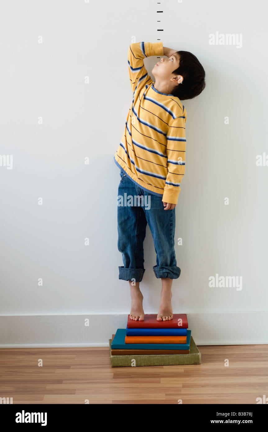 Asian boy standing on books en face de marqueurs de la hauteur Banque D'Images