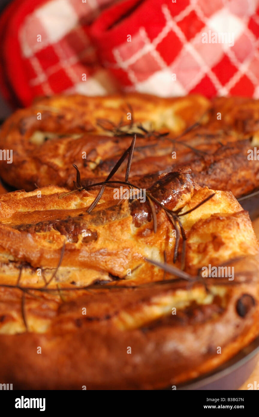 Plat anglais traditionnel Toad-dans-le-trou (saucisses dans la pâte) avec une croix rouge et blanc gant four vérifié comme arrière-plan. Portrait Banque D'Images