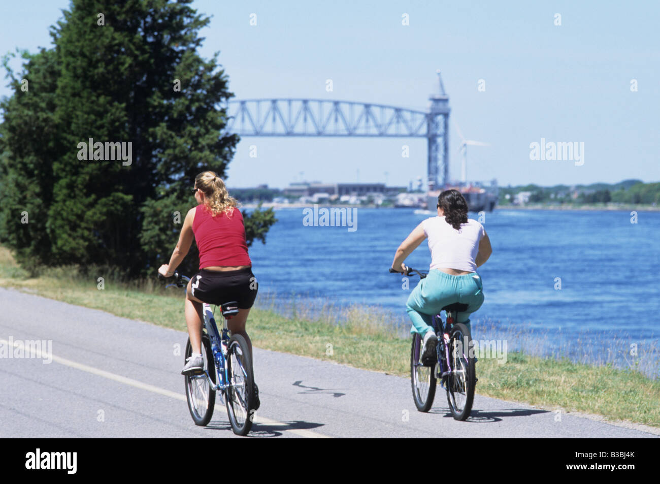 2 Deux personnes femmes équitation à vélo le long du Canal de Cape Cod avec pont à distance Banque D'Images