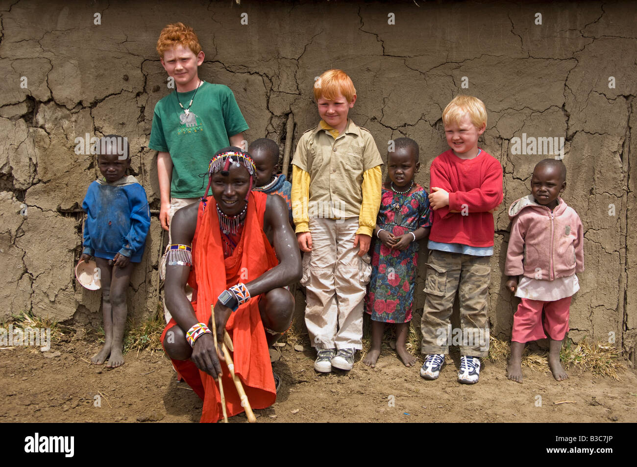 Kenya, Masai Mara National Reserve. Au cours d'une visite d'une manyatta Masaï, les enfants sur un safari familial posent pour une photo avec Banque D'Images