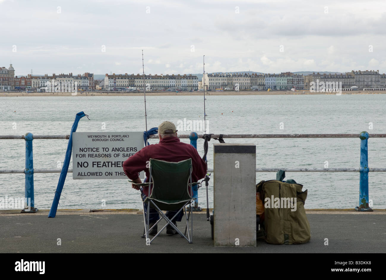 Détente pêcheur dans son fauteuil et profiter de la vue du front de mer dans la pêche à la ligne à la fin du Port Arm Banque D'Images