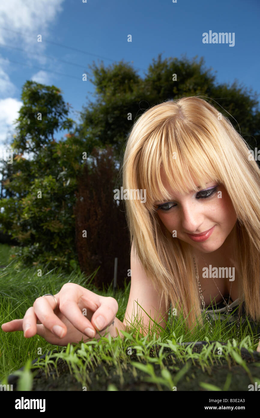 Jeune femme aux cheveux blonds fin de l'adolescence au début de la vingtaine qui tend un bac de persil herb semis dans un jardin Banque D'Images