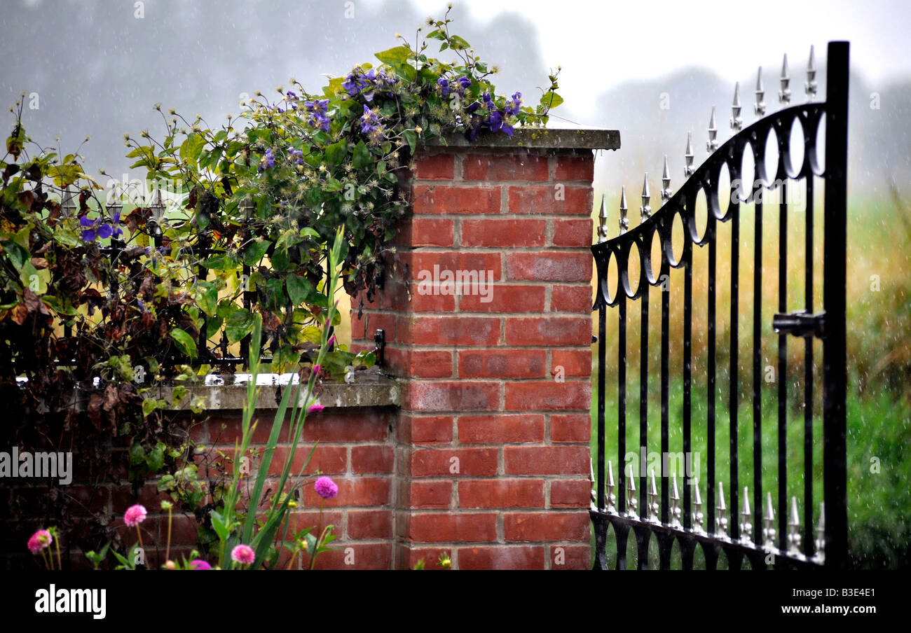 Ouvrez la porte en fer forgé jardin décoratif hanging off Pilier en brique avec mur de brique à côté couvert de clématite Banque D'Images