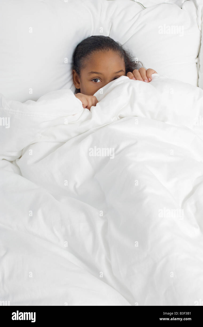 Girl (7-9) se cachant sous les couvre-lits, portrait Banque D'Images