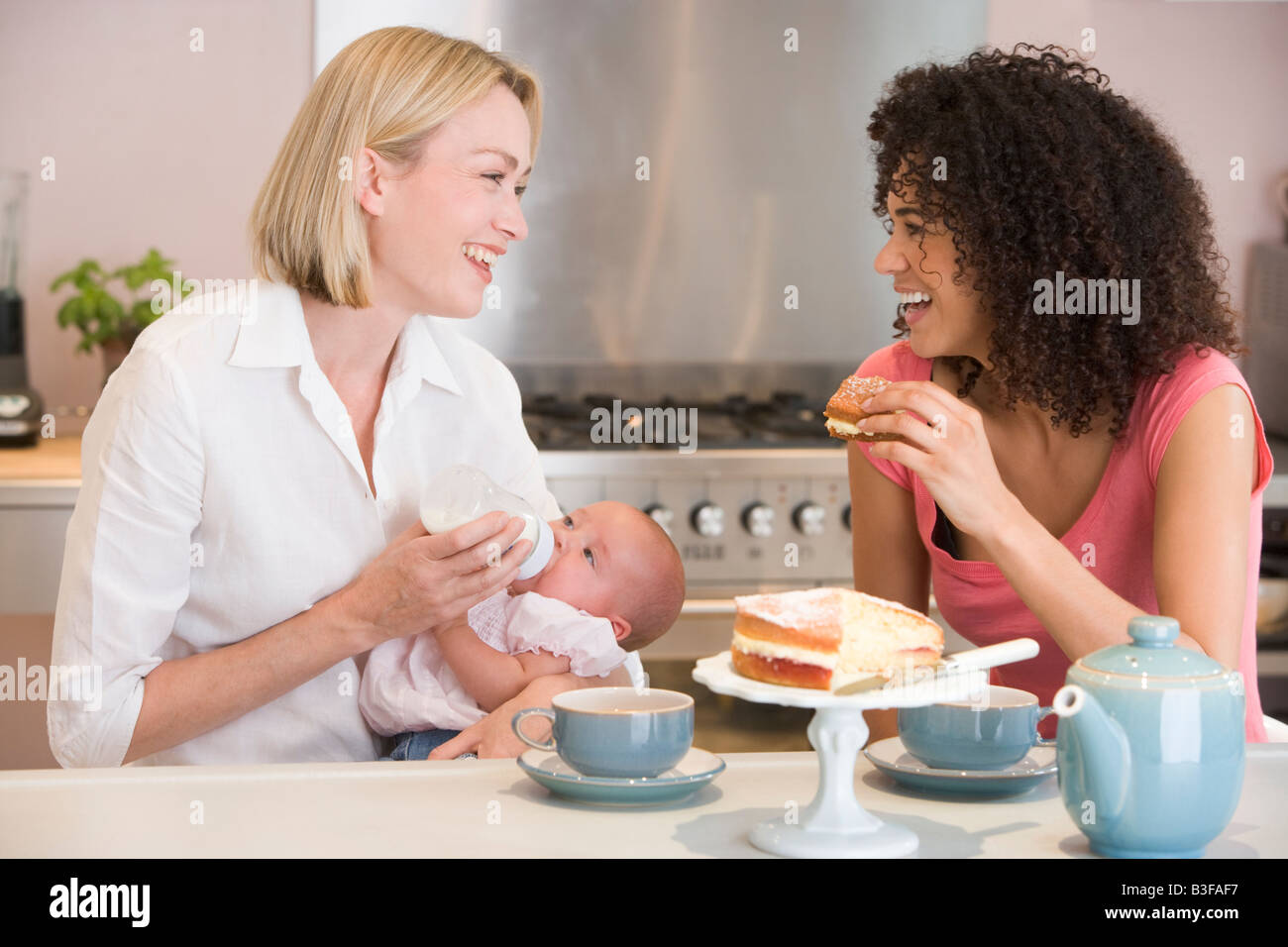 Mère et bébé en cuisine avec ami eating cake and smiling Banque D'Images