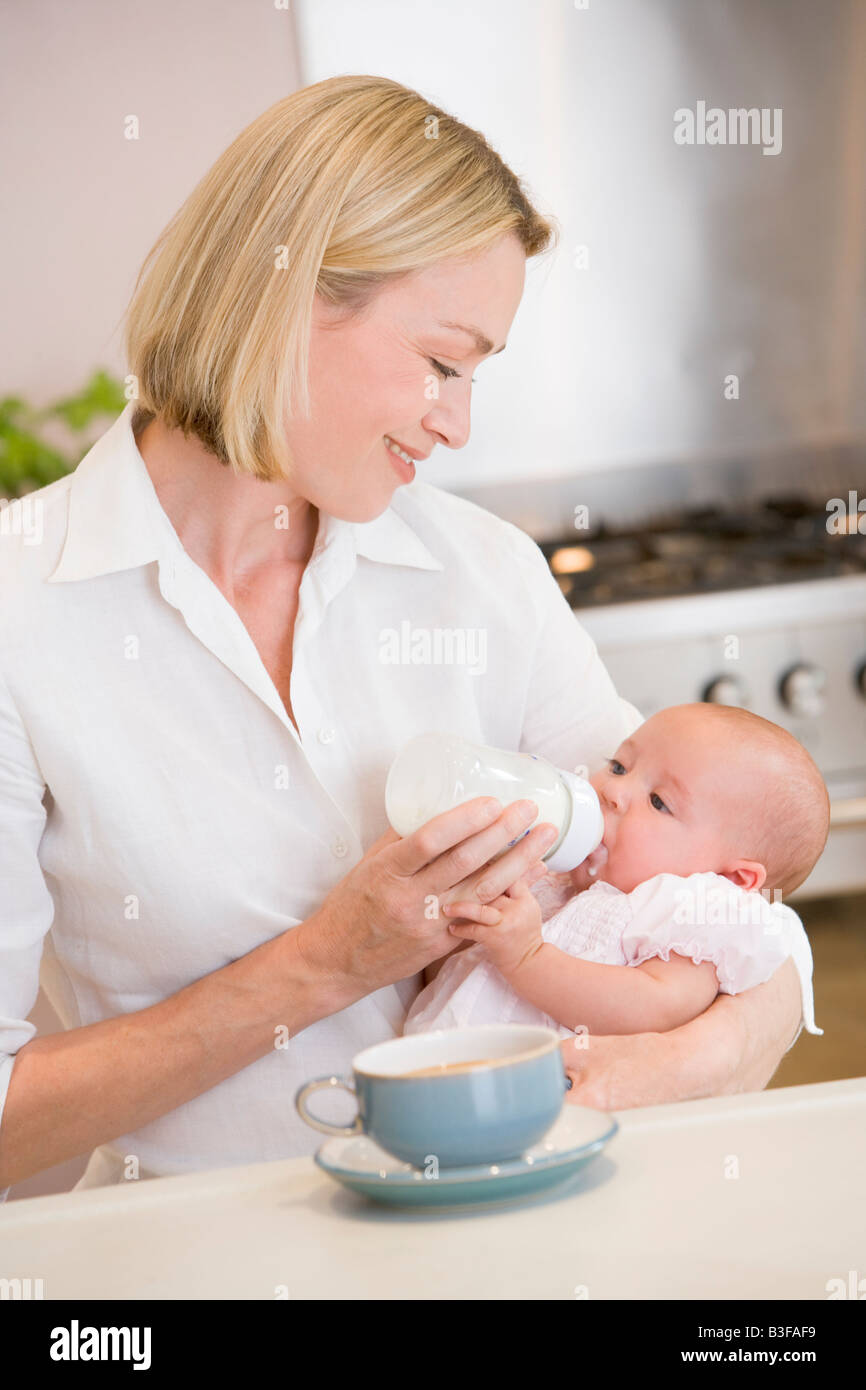 Mère de nourrir bébé dans la cuisine avec cafetière smiling Banque D'Images