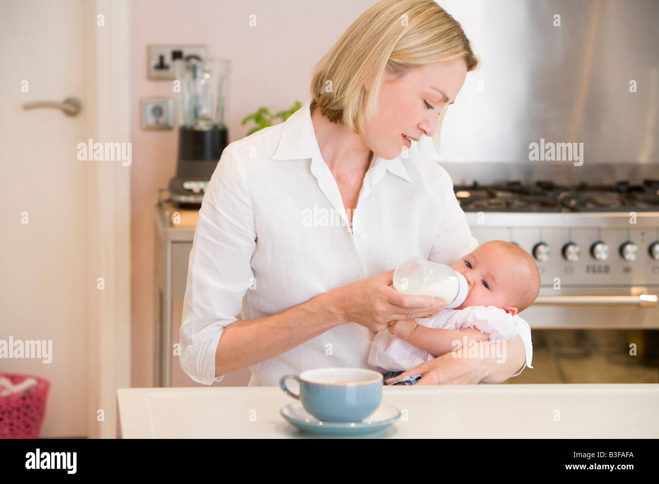 Mère de nourrir bébé dans la cuisine avec cafetière Banque D'Images