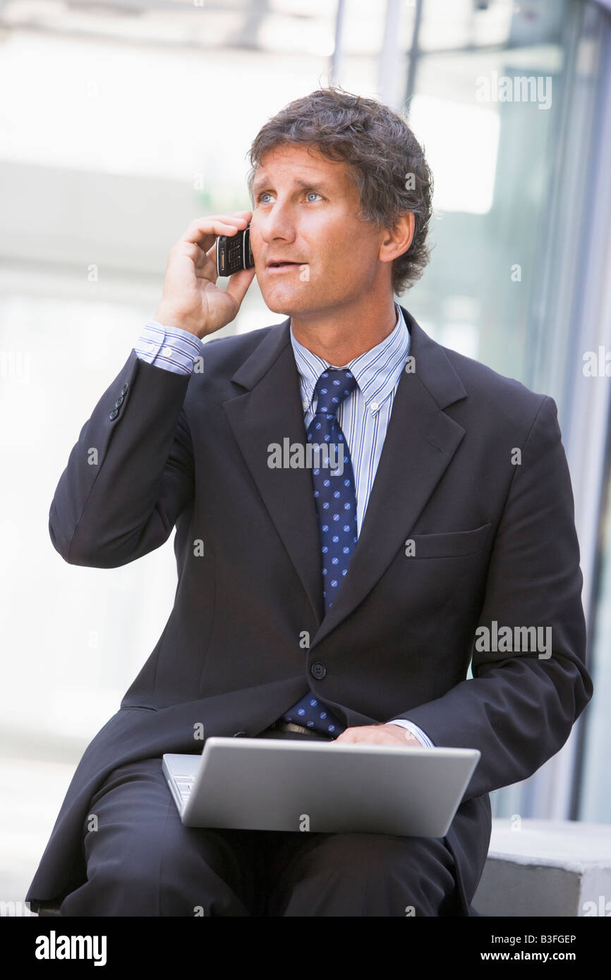 Businessman sitting in office lobby with laptop using cellular phone Banque D'Images