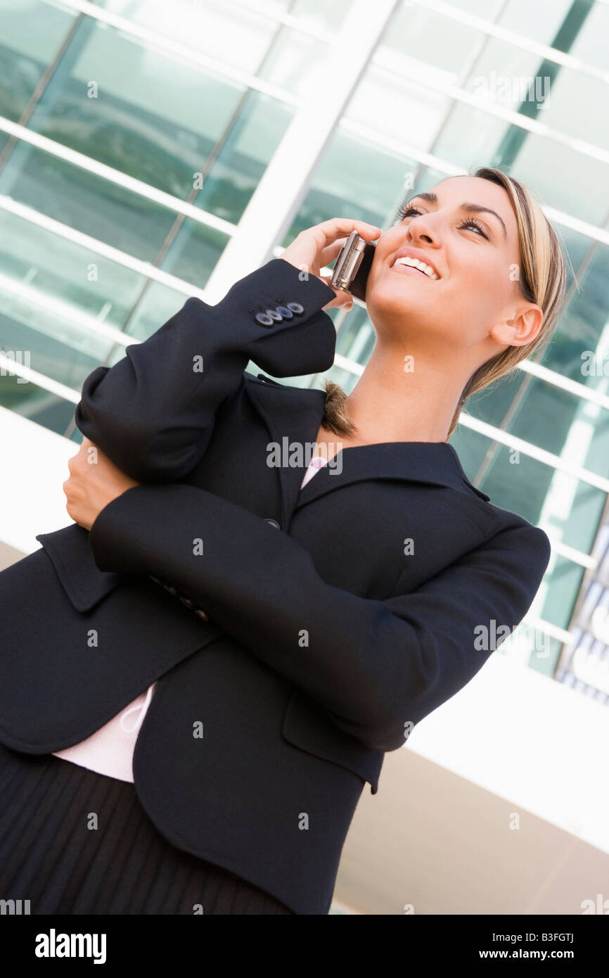 Businesswoman standing outdoors using cellular phone and smiling Banque D'Images