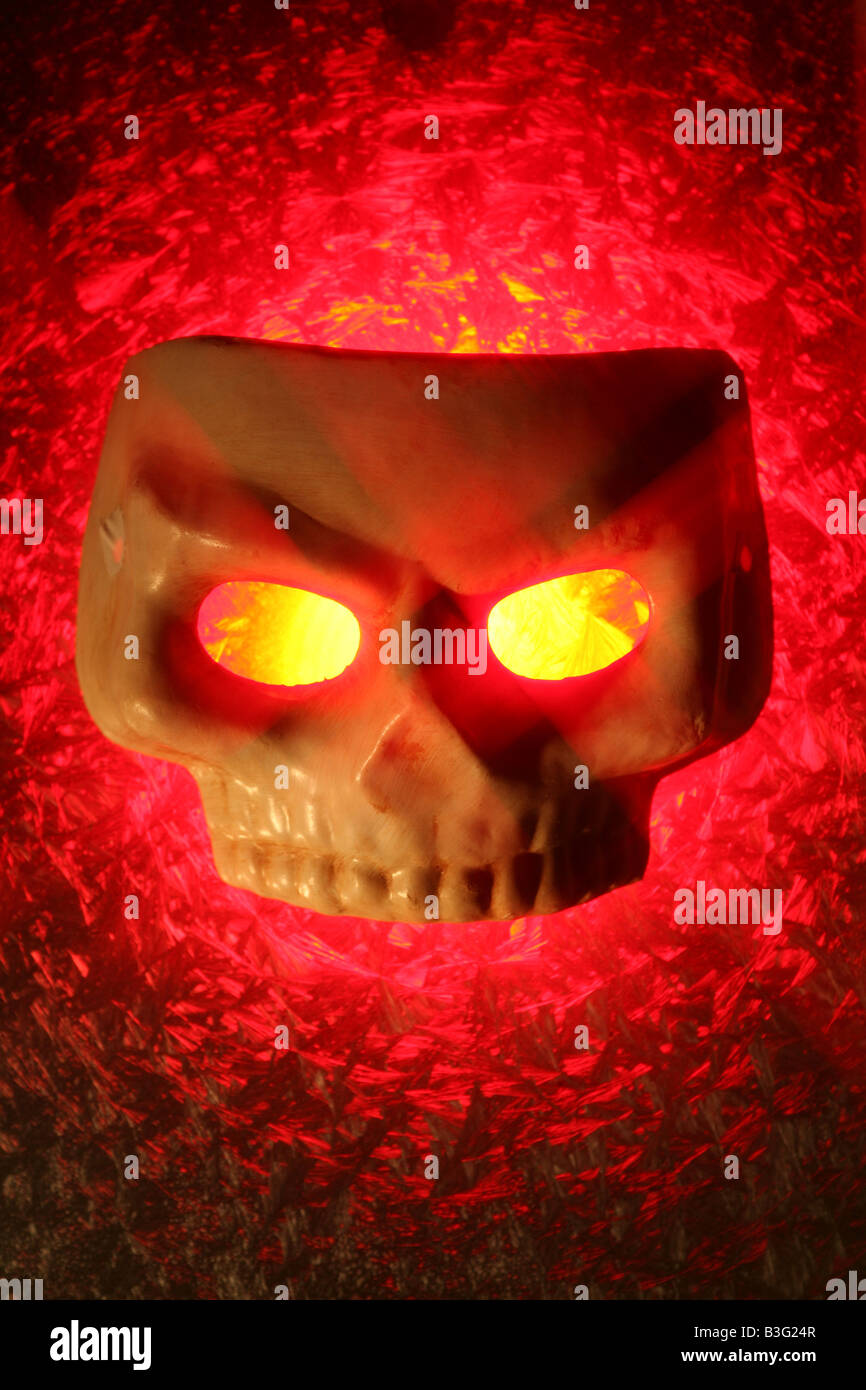 Un masque de crâne avec des yeux jaune brillant et l'arrière-plan lumineux rouge Banque D'Images