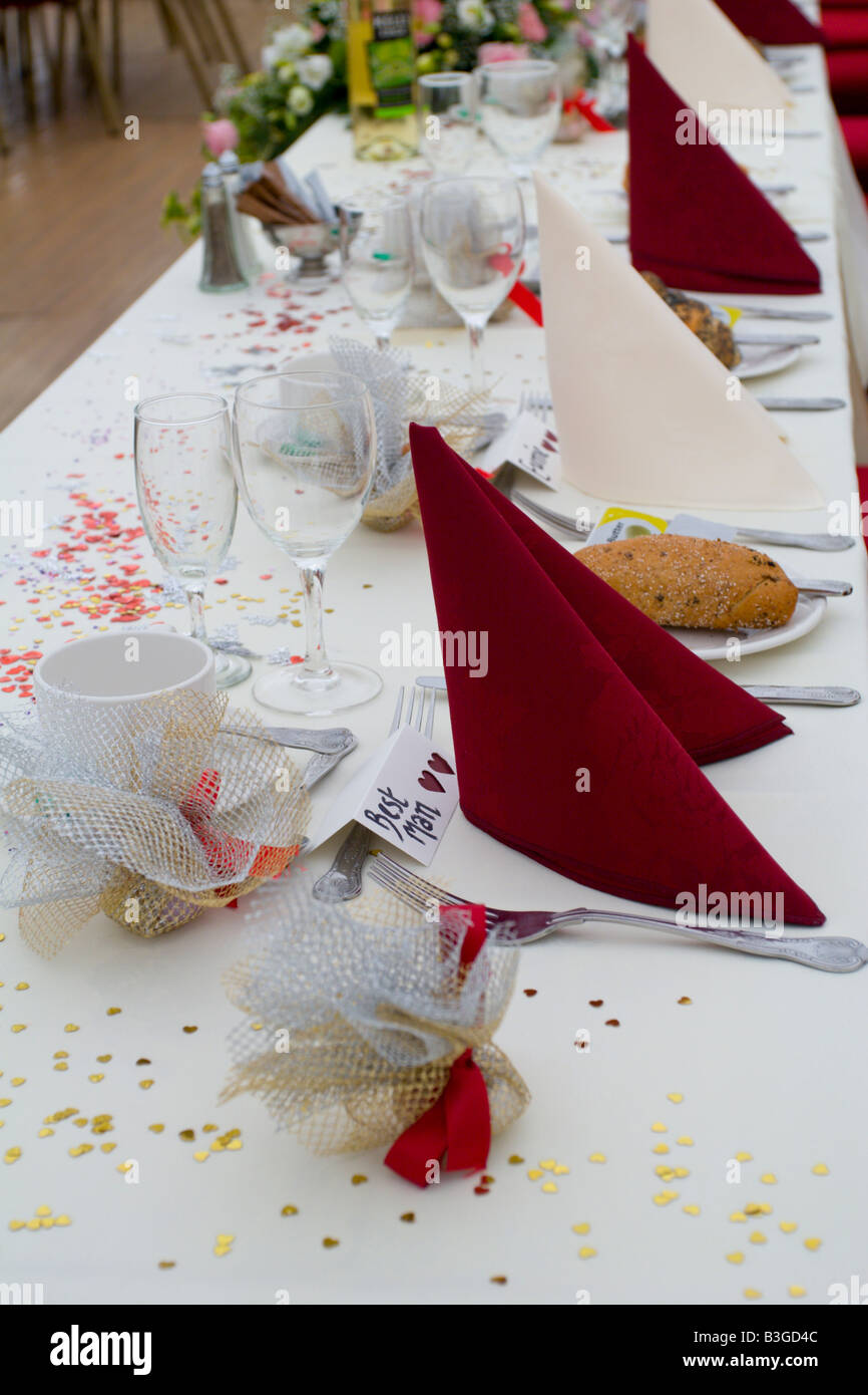 Une table de mariage décoré avec des serviettes de table rouge, faveurs et confettis. aussi les noms de lieu sur la table dont une pour le meilleur homme. Banque D'Images