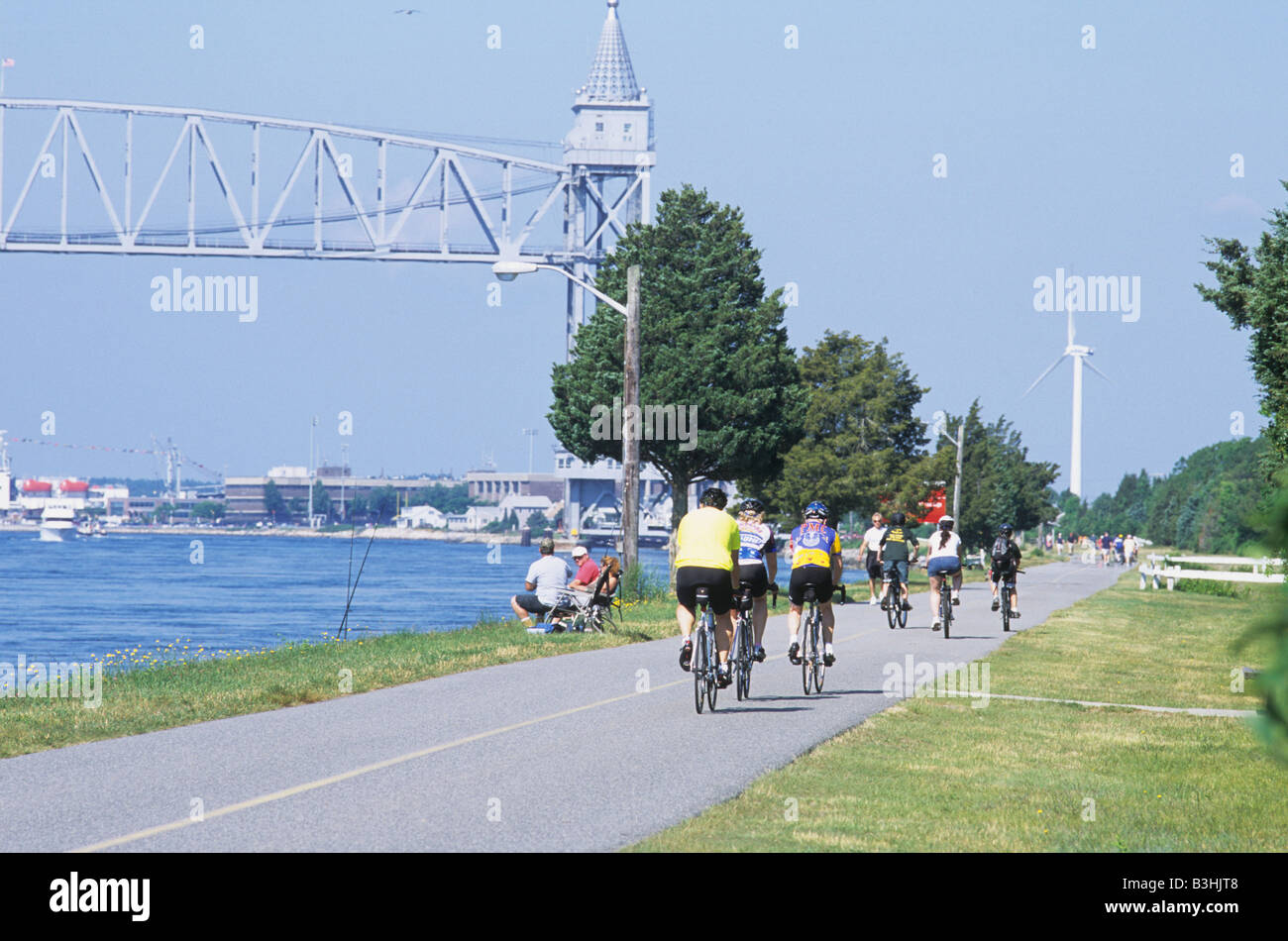 Groupe de personnes de couleur sur les vélos et assis le long de Cape Cod Canal avec pont de chemin de fer et d'éoliennes en été. Banque D'Images