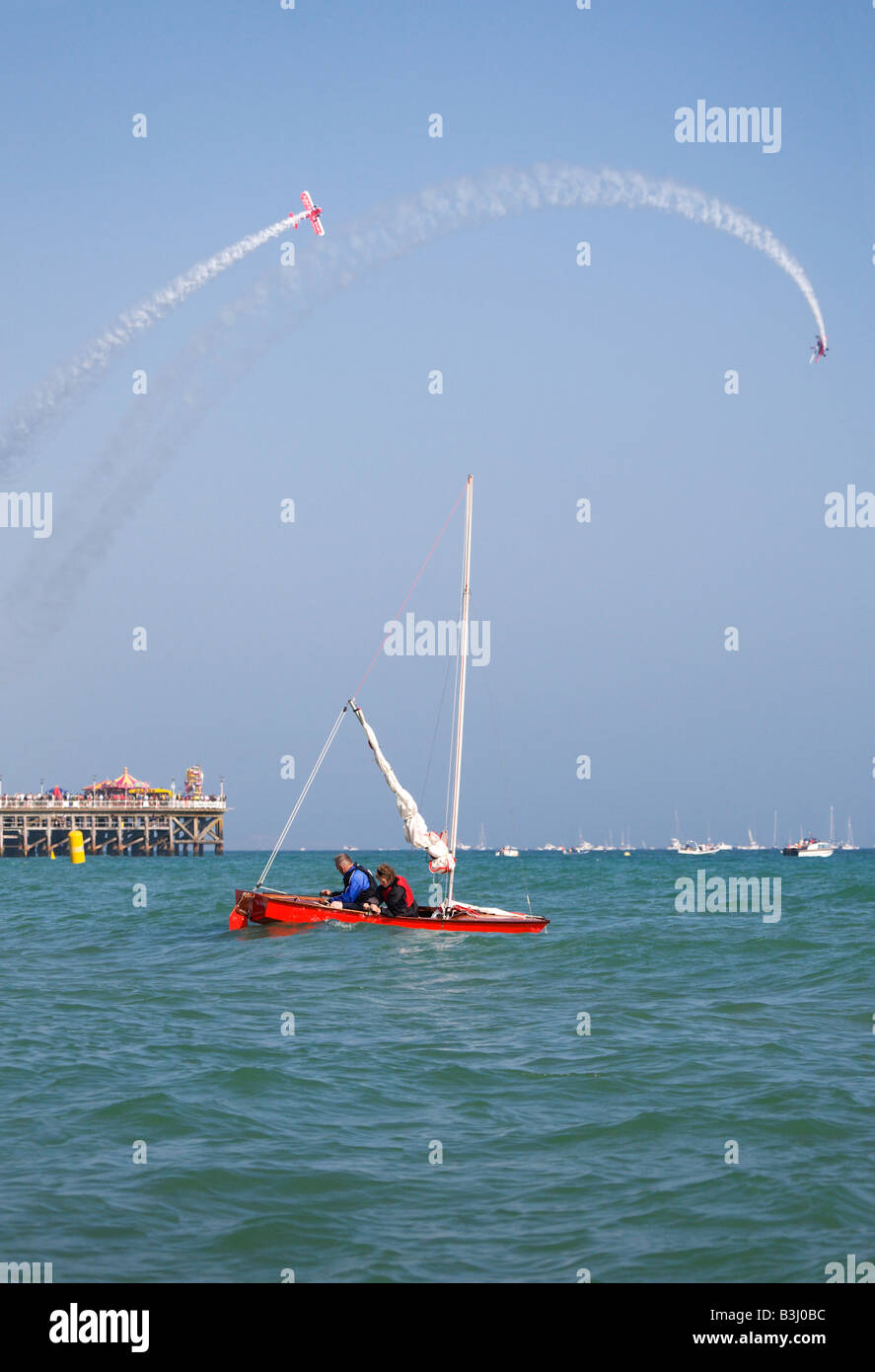 Un couple dans un bateau à voile au large de la plage de Bournemouth, Bournemouth durant la fête de l'air. Biplan afficher sur la jetée. Le Dorset. Banque D'Images