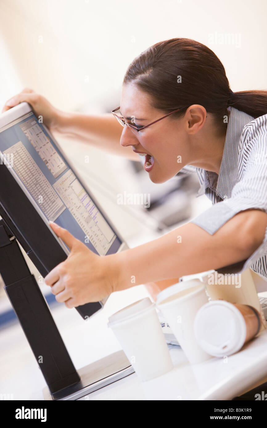 Woman in computer room saisissant son moniteur et crier Banque D'Images