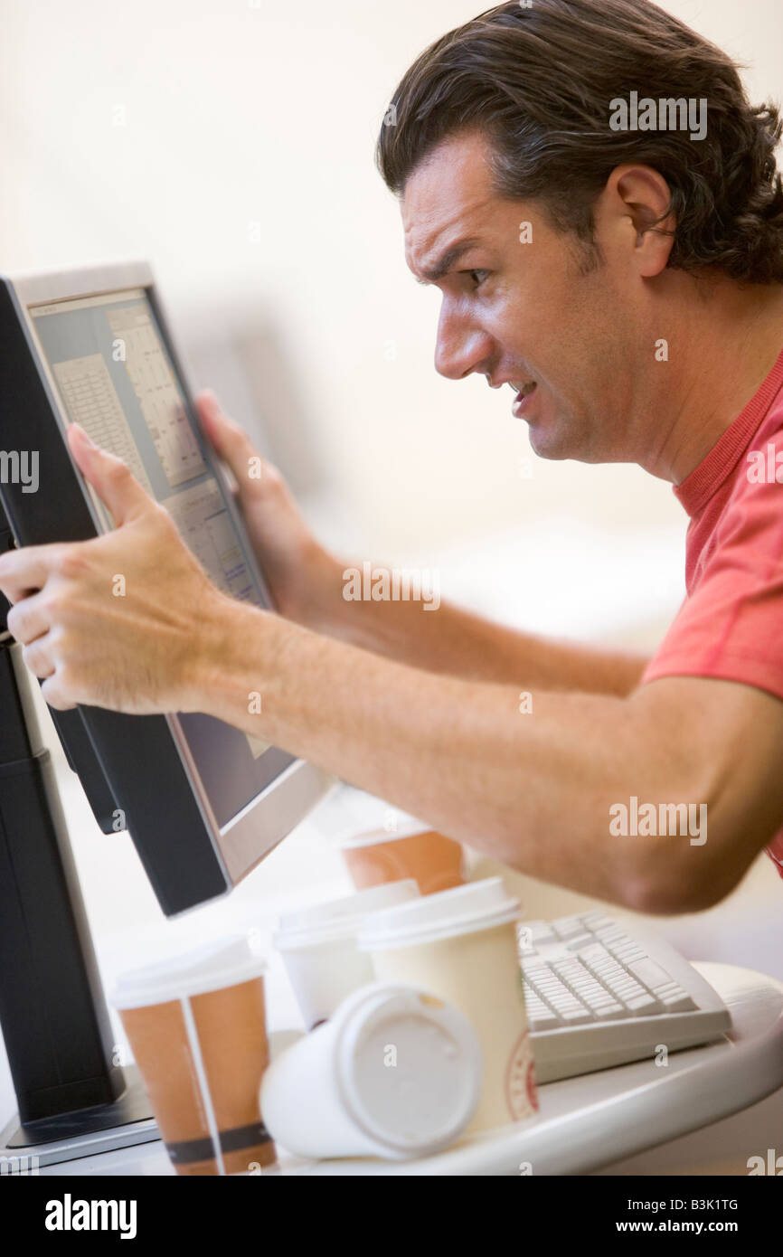 L'homme dans la salle informatique avec de nombreuses tasses de café vide attrapant sa frustration moniteur Banque D'Images
