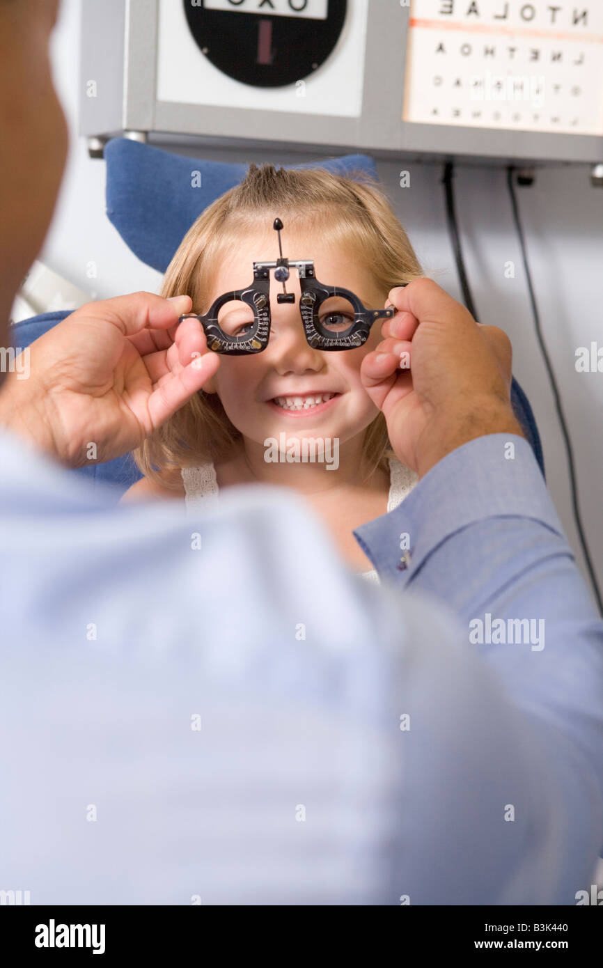 Optométriste dans la salle d'examen avec jeune fille en chaise smiling Banque D'Images