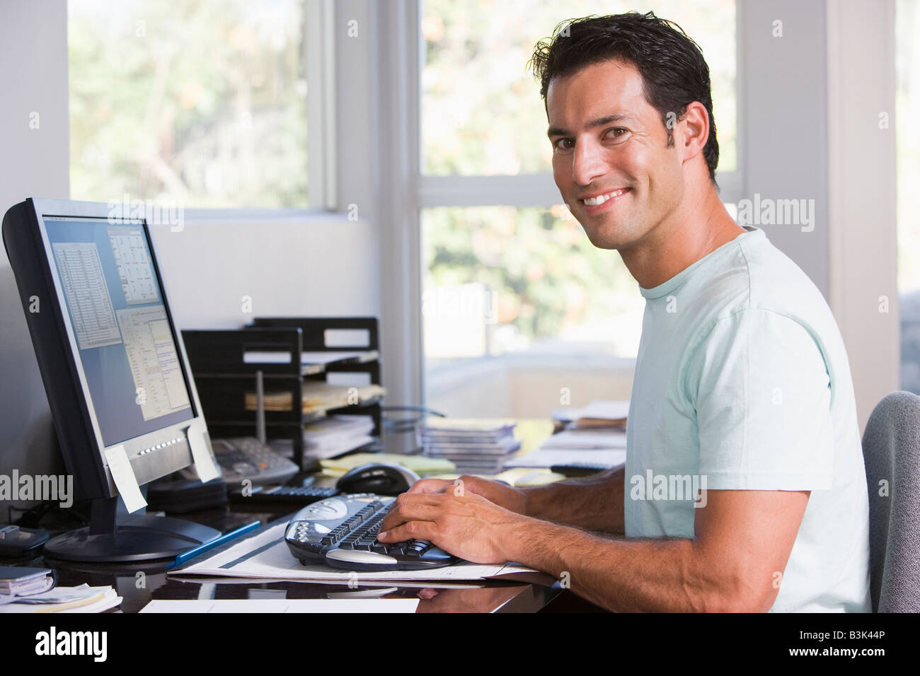 L'homme à l'aide d'un ordinateur de bureau à domicile et souriant Banque D'Images