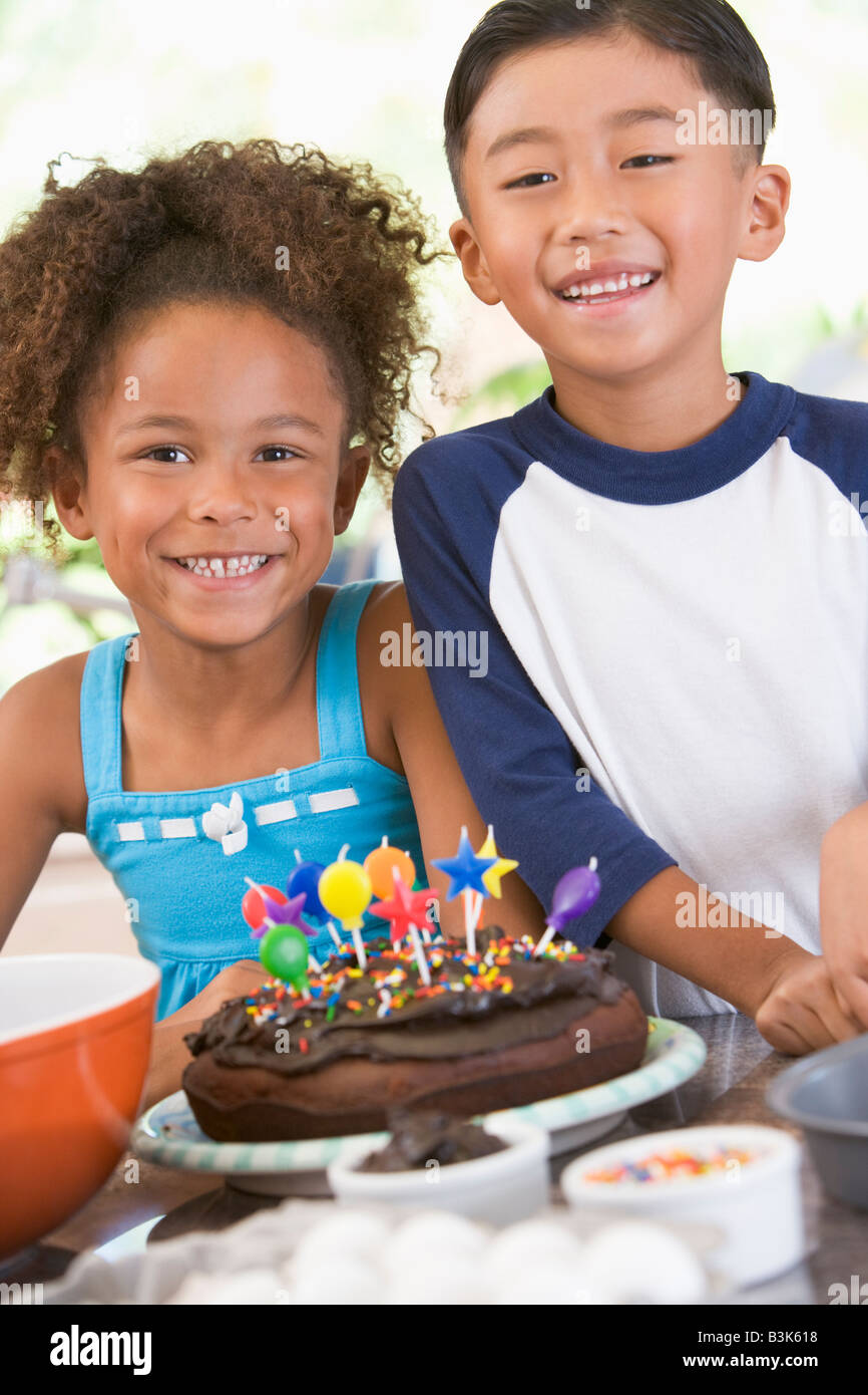 Deux enfants en cuisine avec gâteau d'anniversaire, smiling Banque D'Images