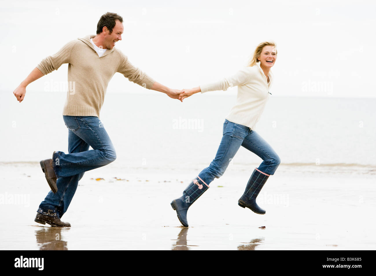 Couple running on beach holding hands smiling Banque D'Images