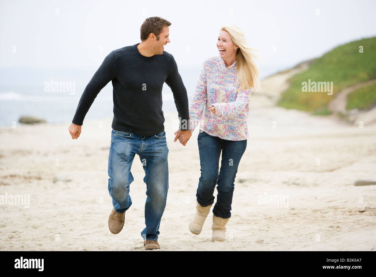 Couple running at beach holding hands smiling Banque D'Images