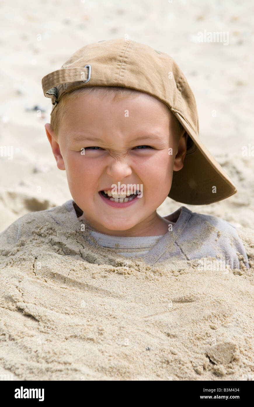 Un petit garçon de 8 ans, portant une casquette s'amuse après avoir été  enterré jusqu'au cou dans le sable sur la plage Photo Stock - Alamy