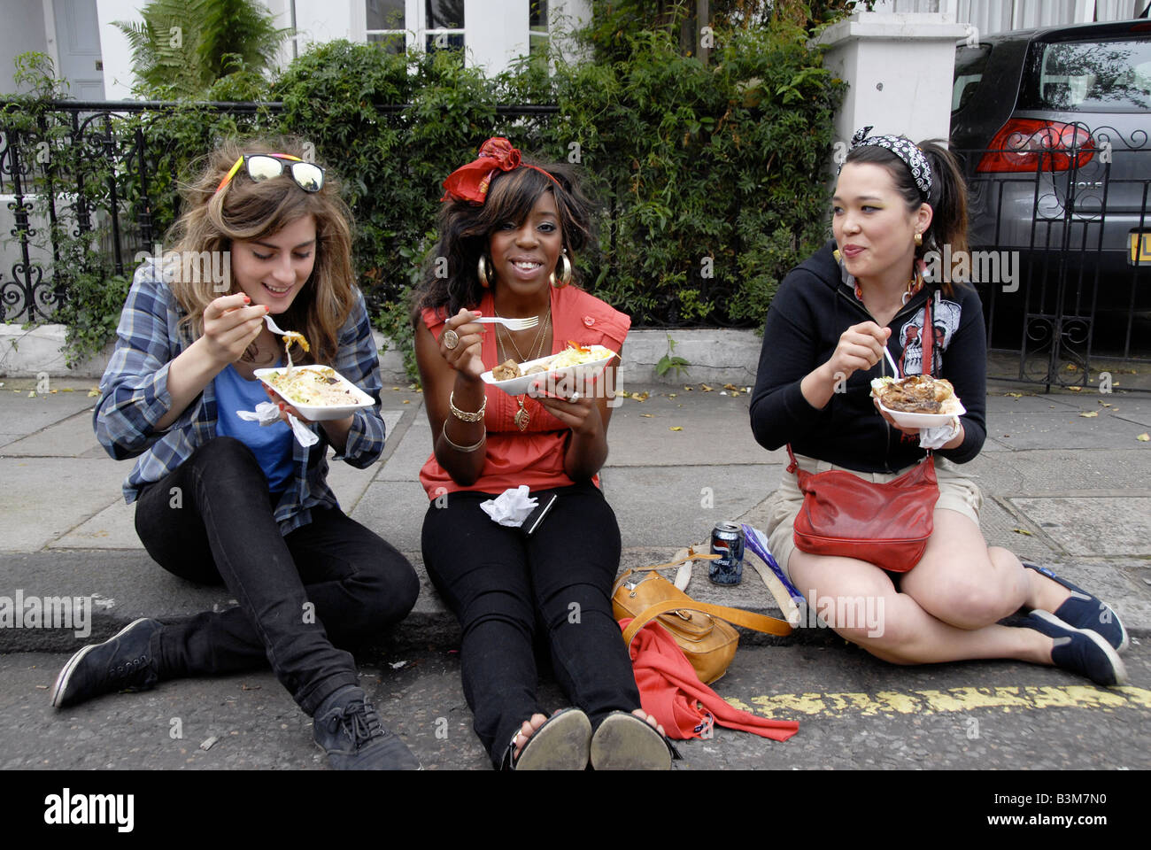 Trois jeunes femmes assises sur la chaussée eating fast food à emporter Banque D'Images