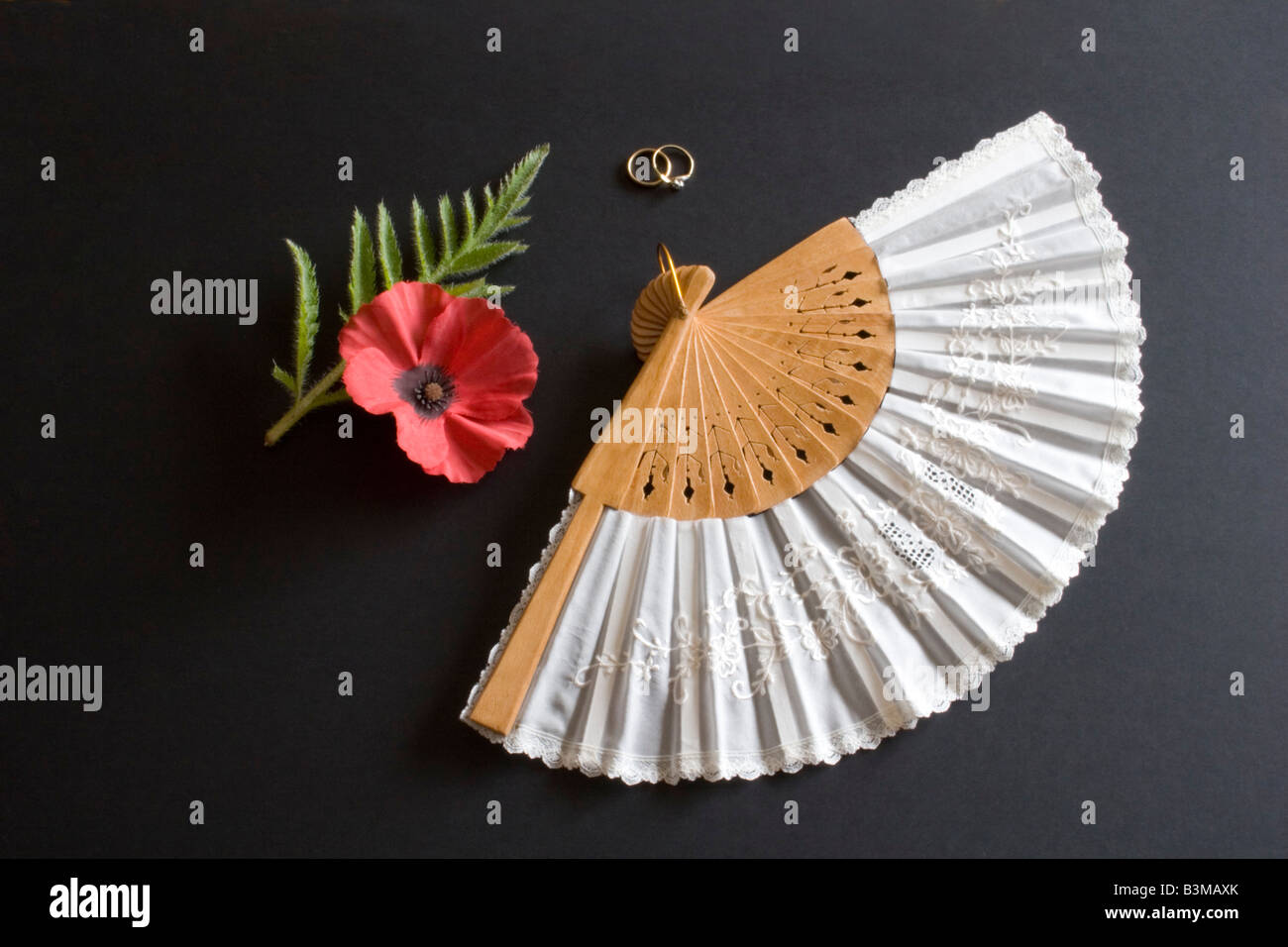 Ventilateur pliant blanc Oriental sur fond noir avec des anneaux et pavot rouge Banque D'Images