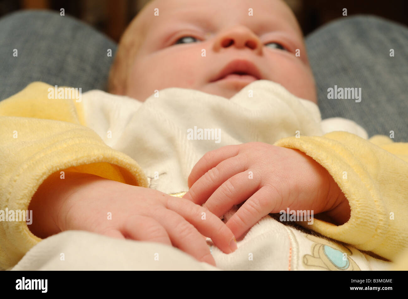 Un bébé de trois mois dans une tenue jaune et blanc, avec ses mains le principal point d'intérêt Banque D'Images