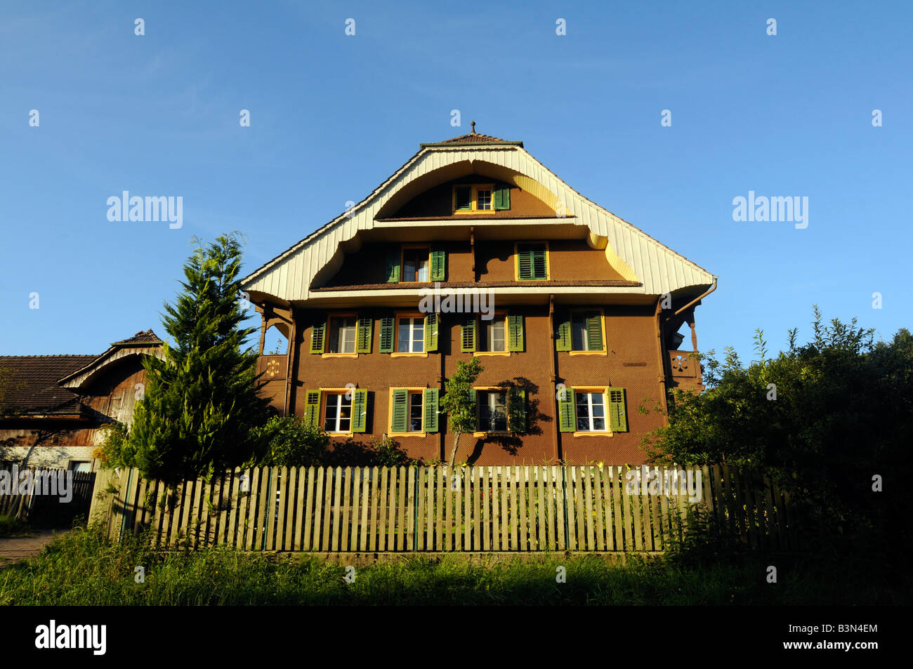 Une maison suisse typique dans un cadre rural, avec arbres, montagnes, et drapeau national ; photo prise en Suisse centrale Banque D'Images