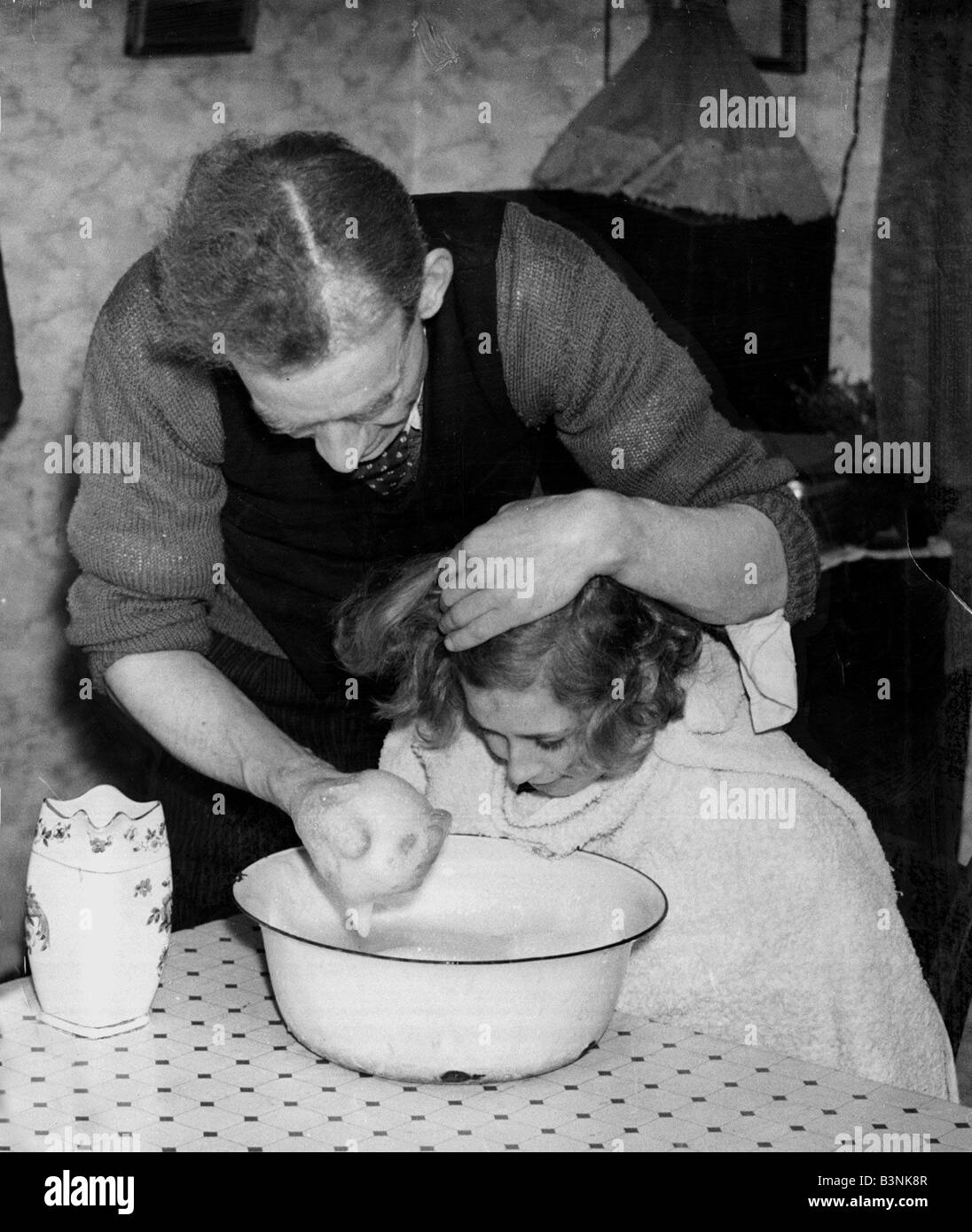 Un homme lave sa fille et les cheveux à l'aide d'eau savonneuse dans un bol dans leur salon 1937 Février 1930 père ménage fille de parent Banque D'Images