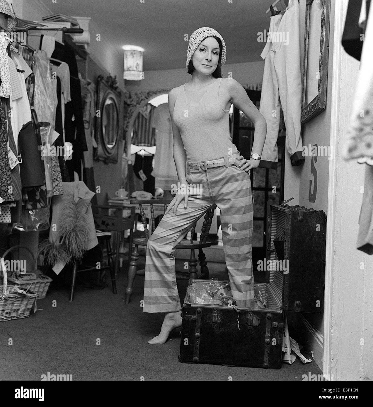 Swinging Sixties Fashion Juillet 1965 Jackie Cryer assis dans l'Épice n° 1 Boutique à Knightsbridge essayer de poser dans des tenues sur le pantalon à rayures et un cavalier portant un chapeau également entouré par des rails de vêtements Banque D'Images