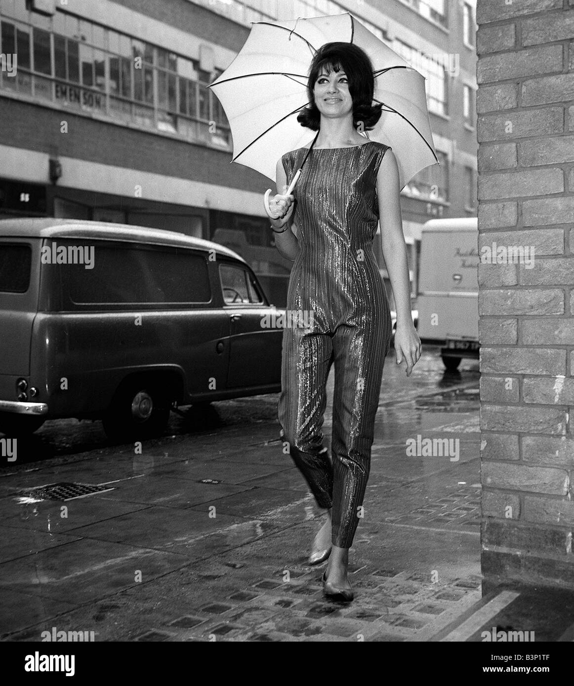 1960 Vêtements Mode Avril 1962 Eastcastle Street Londres W1 Modèle Gay-Bava 21 photographié portant une tenue d'une collection par Emcar Casuals Clothing Company une soirée tenue appelée Goldrush il peut aussi être décrit comme un catsuit holding an umbrella Banque D'Images