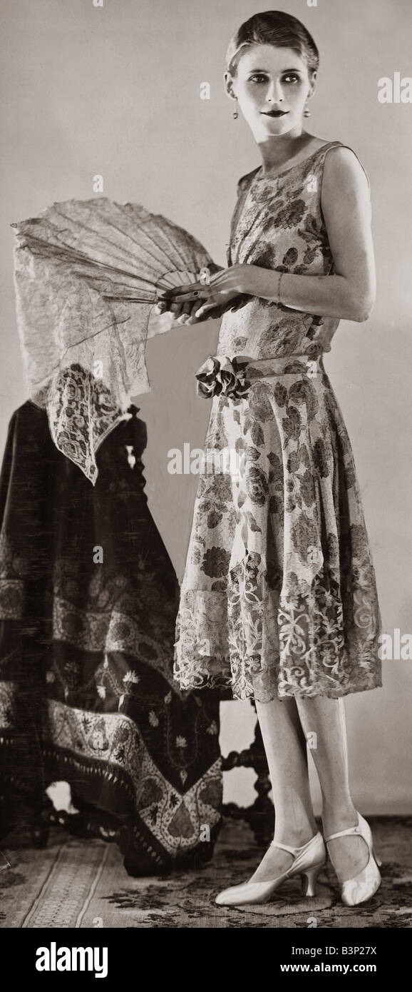 Une femme en blanc et or robe de soirée de brocart qui dispose d'un corsage serré et l'étroite ceinture et bow devant elle tient un ventilateur dans une main 1926 fashion femme femmes robe de soirée élégante pleine longueur miroir 1920 610 26 Banque D'Images