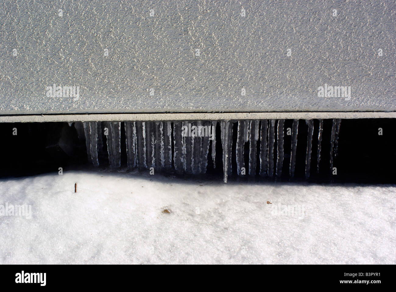 Les glaçons accrocher sur la neige sur un affleurement de bas d'un immeuble. Banque D'Images