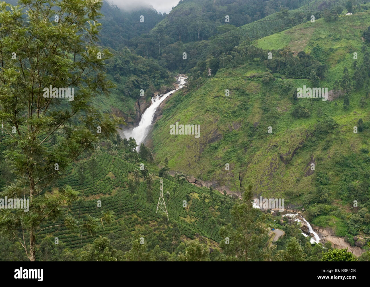 La vue du flux des highlands avec cascade dans la vallée de fermes et de forêts entre les montagnes avec les nuages et la brume sur les crêtes. Banque D'Images