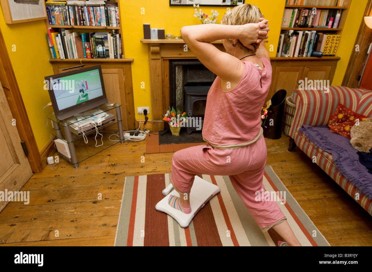 Femme d'âge moyen faire son yoga exercices sur une Nintendo Wii Fit dans le salon de sa maison à la maison, UK Banque D'Images