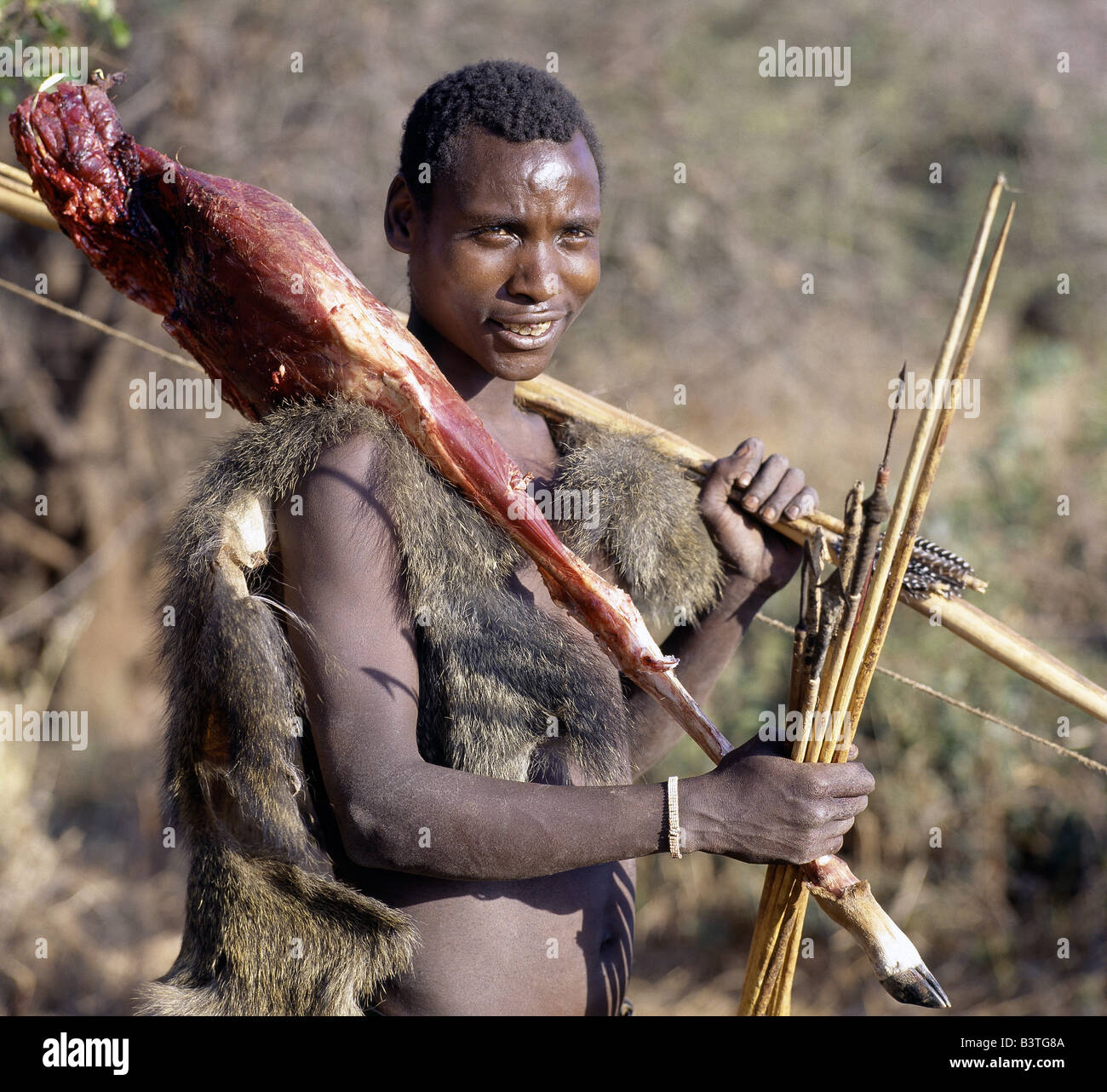 La Tanzanie, le nord de la Tanzanie, le lac Eyasi. Un chasseur Hadza portant un babouin peau retourne au camp avec une gigue d'impala sur son épaule. Il a tué la gazelle avec une flèche à pointe métallique qui avait été trempée dans un poison à action rapide légumes extrait de la rose du désert (Adenium obesum).Les Hadzabe sont une communauté forte de milliers de chasseurs-cueilleurs qui ont vécu dans le bassin du lac Eyasi depuis des siècles. Ils sont l'un des quatre ou cinq sociétés dans le monde qui continuent de gagner leur vie principalement de ressources sauvages.. . Banque D'Images
